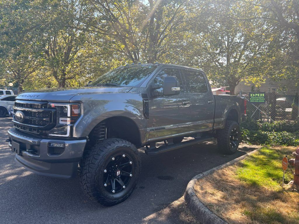 Gray lifted Ford pickup parked on a driveway under trees with sunlight filtering through branches