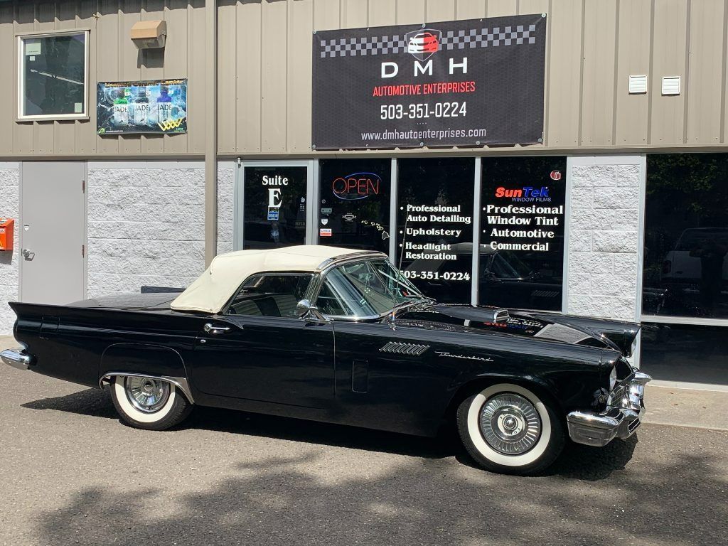 Black classic convertible parked outside a DMH auto shop storefront.