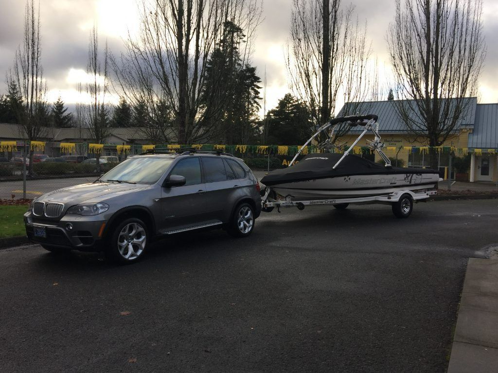 Gray SUV towing a small boat trailer in a wet parking lot at dusk