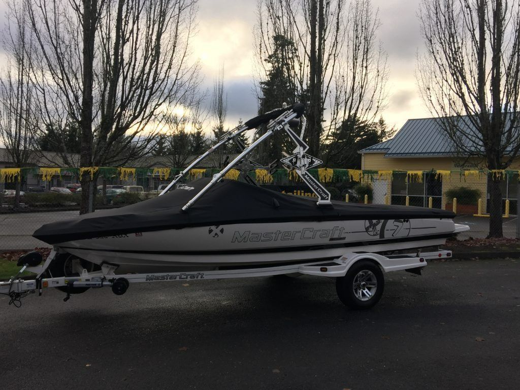 White and black speedboat on a trailer parked outdoors at dusk with bare trees and a gazebo in the background