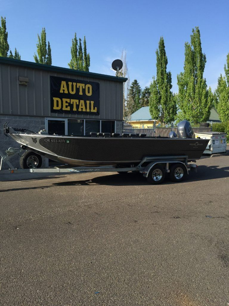 Black boat on a trailer parked outside an auto detail shop on a sunny day