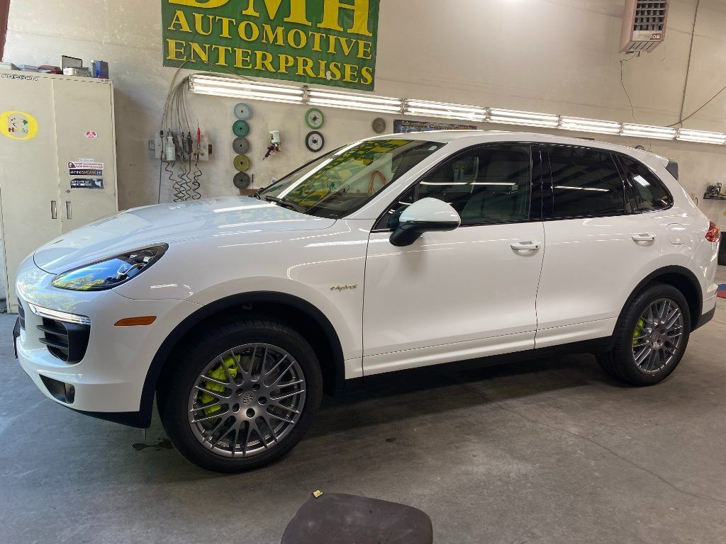 White Porsche SUV in a garage showroom, side view with aftermarket wheels and green brake calipers