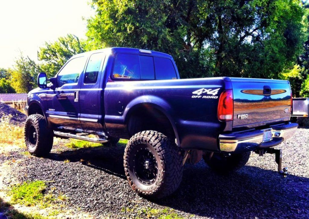 Lifted purple pickup truck parked on gravel near trees, side view