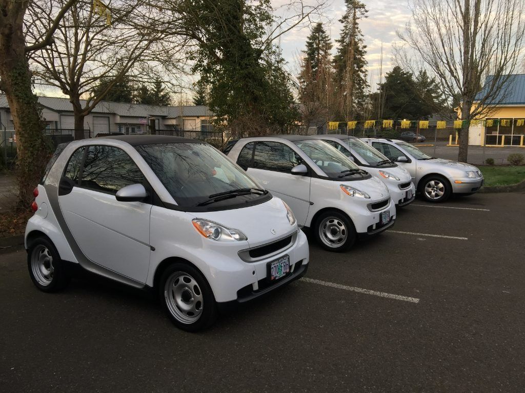 Small silver Smart cars parked in a row in a lot on an overcast day
