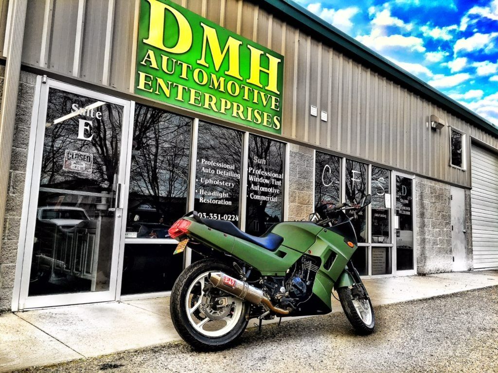 Green sport motorcycle parked outside DMH Automotive Enterprises storefront.
