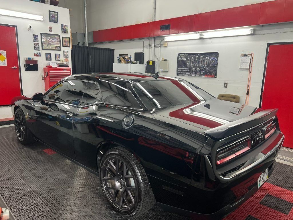 Black sports car in an auto shop garage, viewed from the rear side.