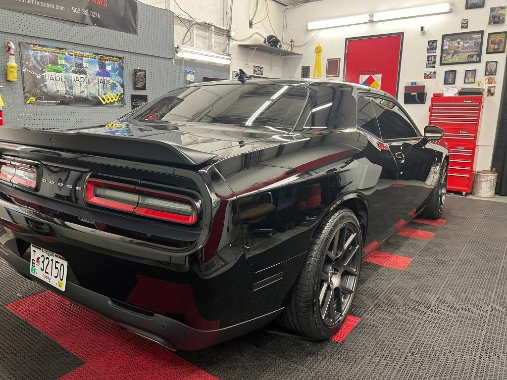 Black Dodge Challenger parked in an auto shop garage with red tool cabinets and work lights