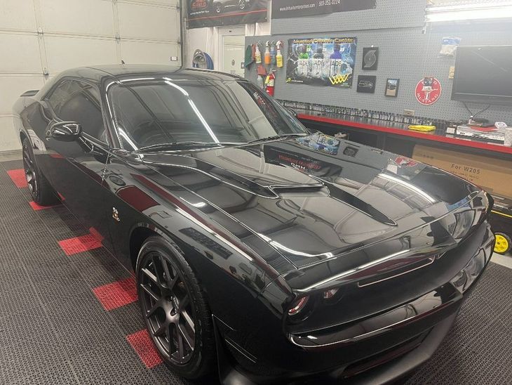 Black sports car in a garage, glossy finish under bright lights with tools and wall decor nearby