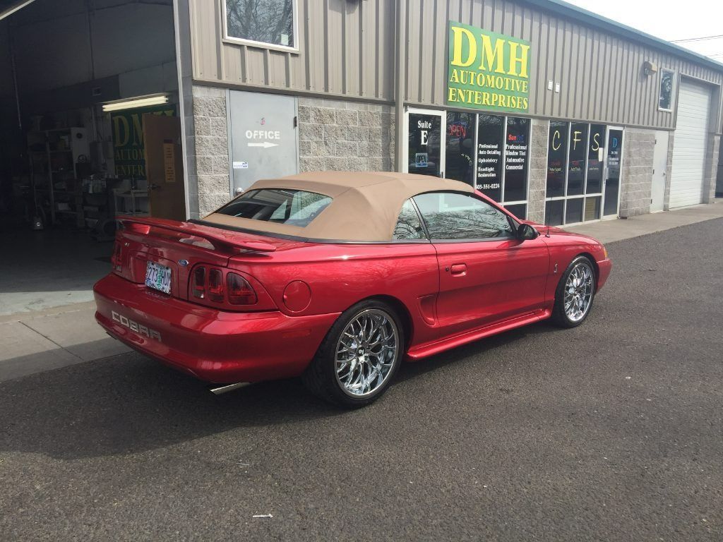 Red convertible sports car parked outside a shop with a green sign.