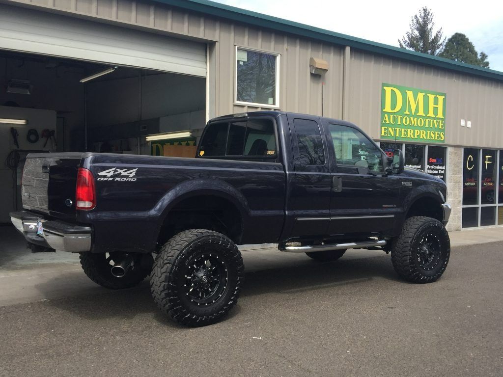 Lifted black pickup truck parked outside an auto shop with a yellow sign.