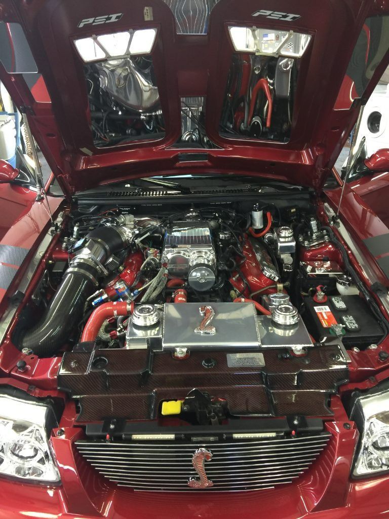 Red sports car with hood open, showing a polished custom engine bay and chrome engine components