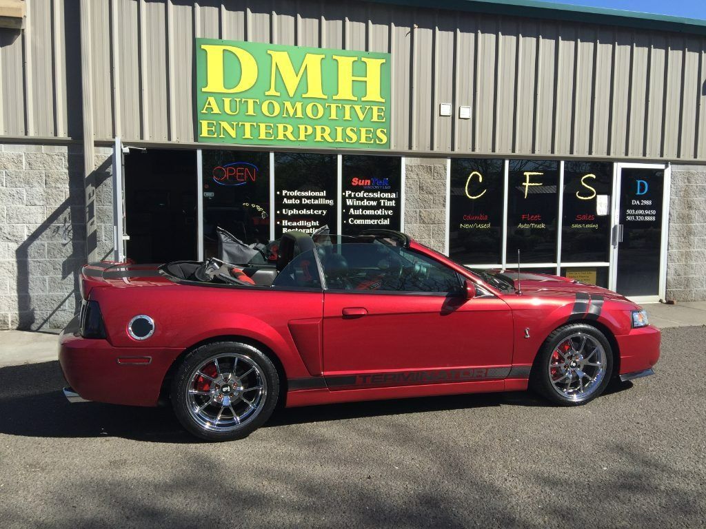 Red convertible sports car parked outside DMH Automotive Enterprises building