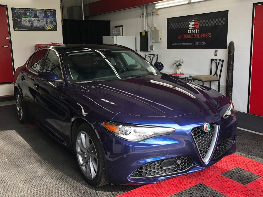 Blue Alfa Romeo sedan in a garage with red-and-black checkered floor mats.