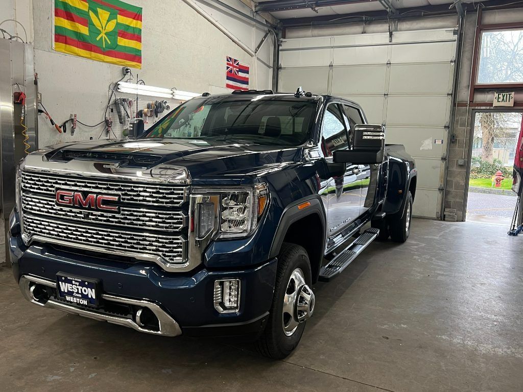 Blue GMC pickup truck parked inside a garage, with a large open door and a flag on the wall.