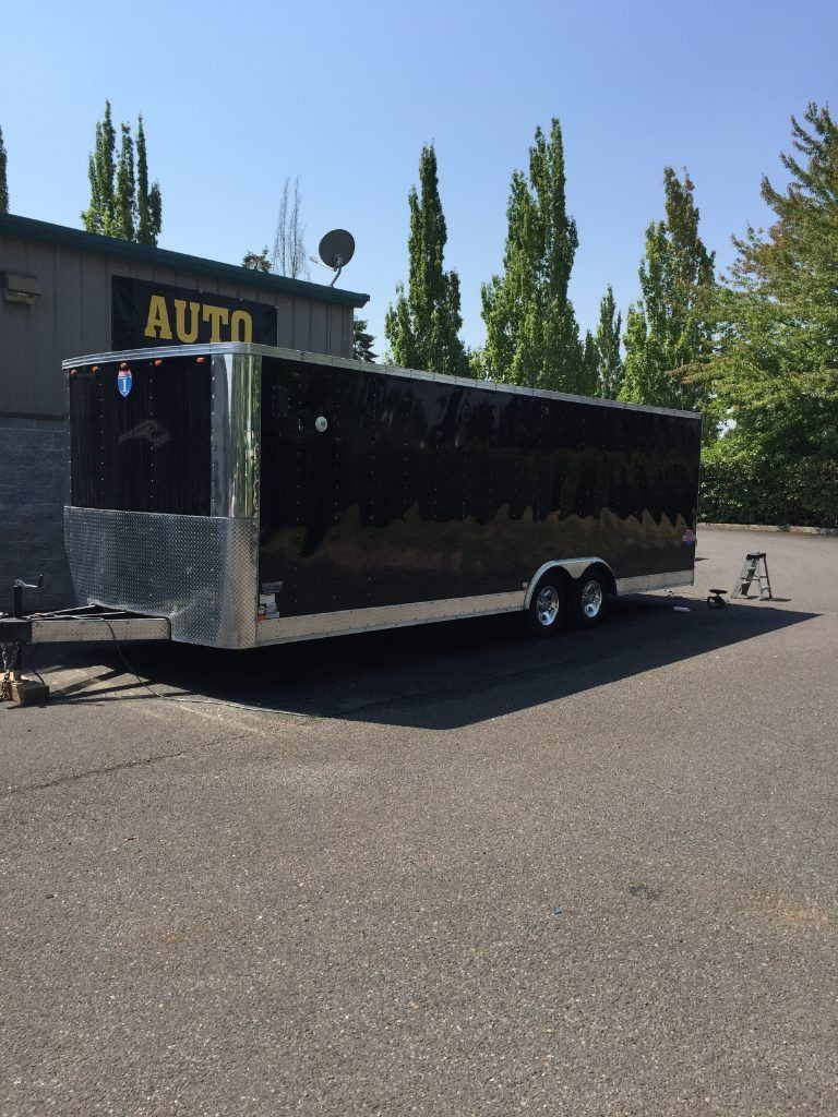 Black enclosed cargo trailer parked on a paved lot beside a building with an AUTO sign.