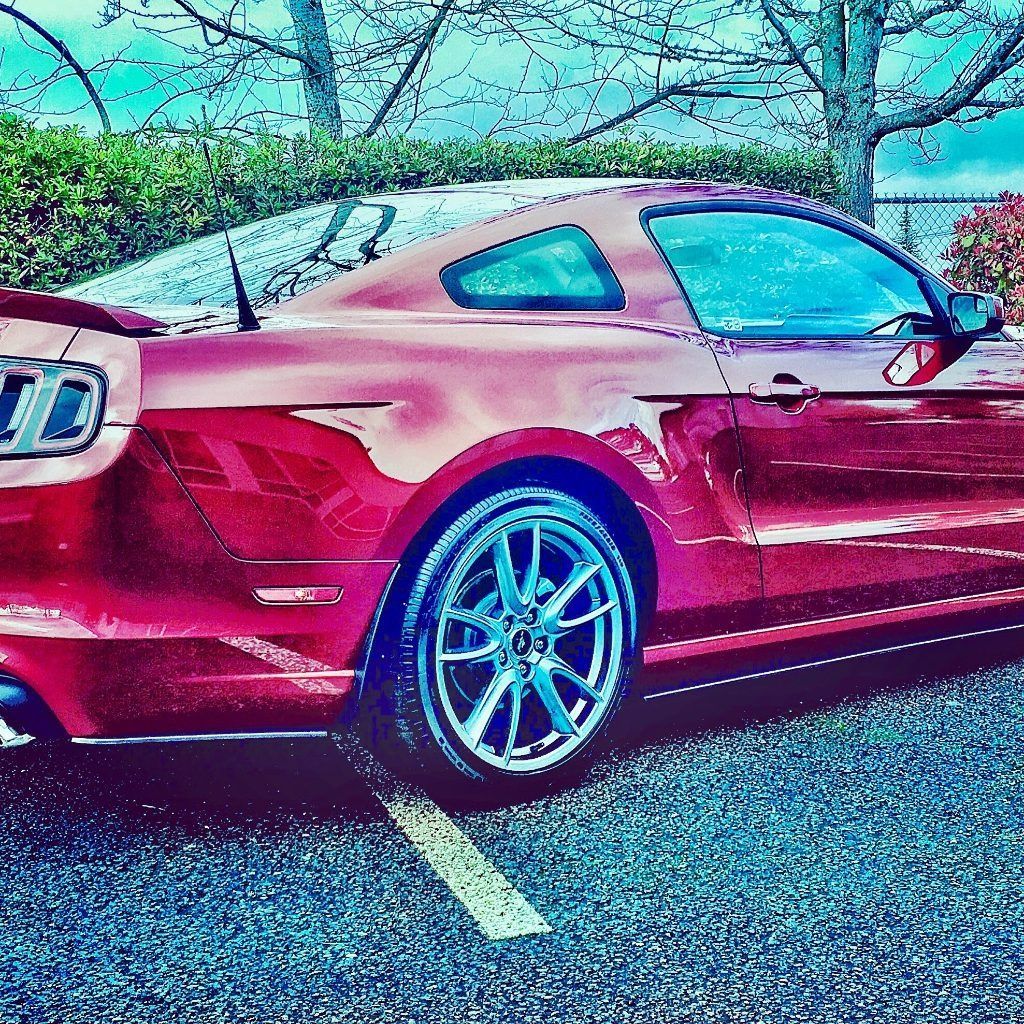 Red sports coupe parked in a lot with a bright, stylized filter and trees in the background.