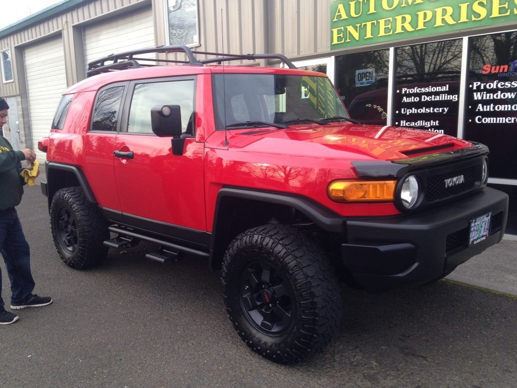 Red off-road SUV with black roof rack and lifted tires parked outside a storefront.