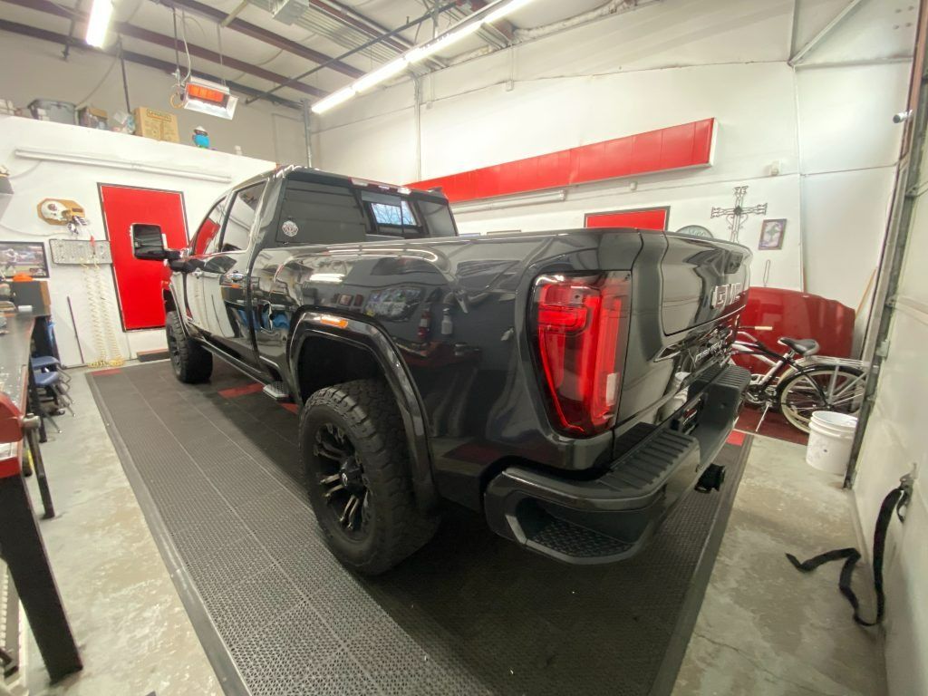 Black pickup truck in an auto shop on a lift, rear three-quarter view, with tools and equipment nearby