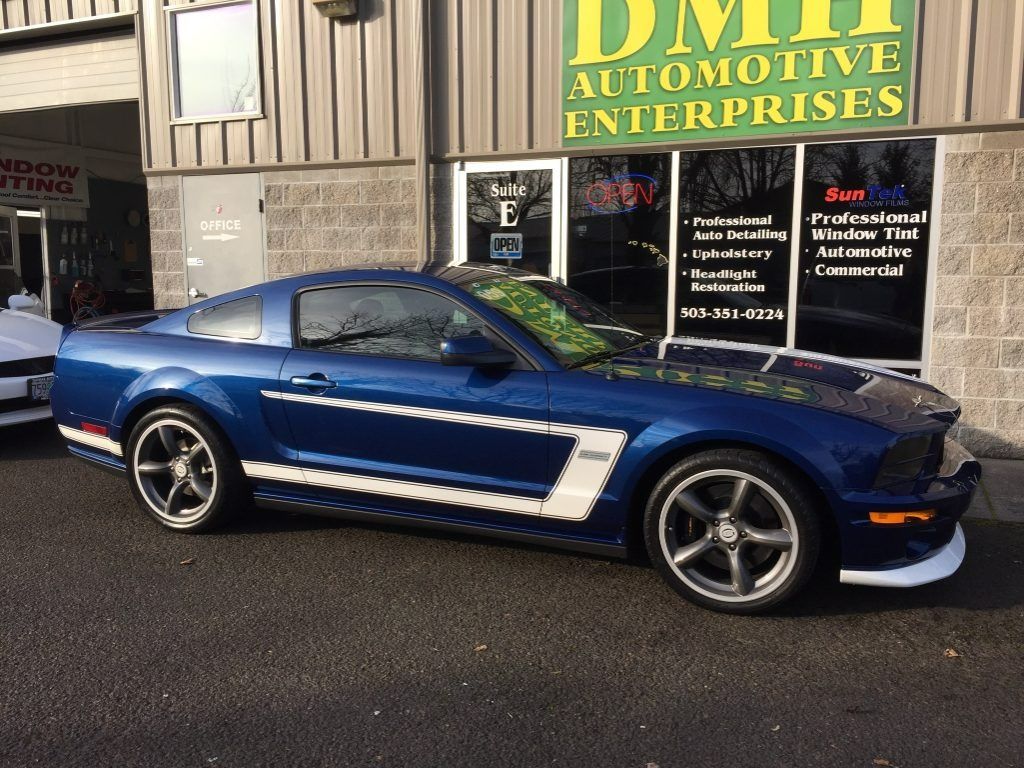 Blue sports car parked outside an automotive shop with a DMI Enterprises sign in the background