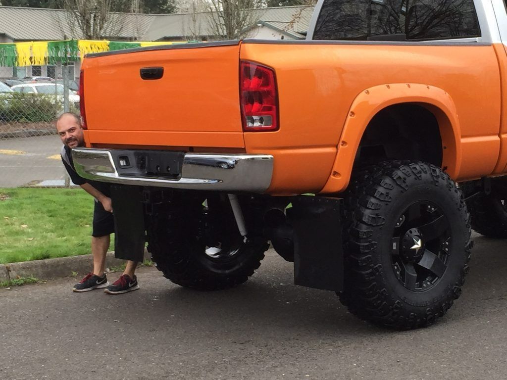 Orange pickup truck with oversized black tires and a person standing behind it on a street