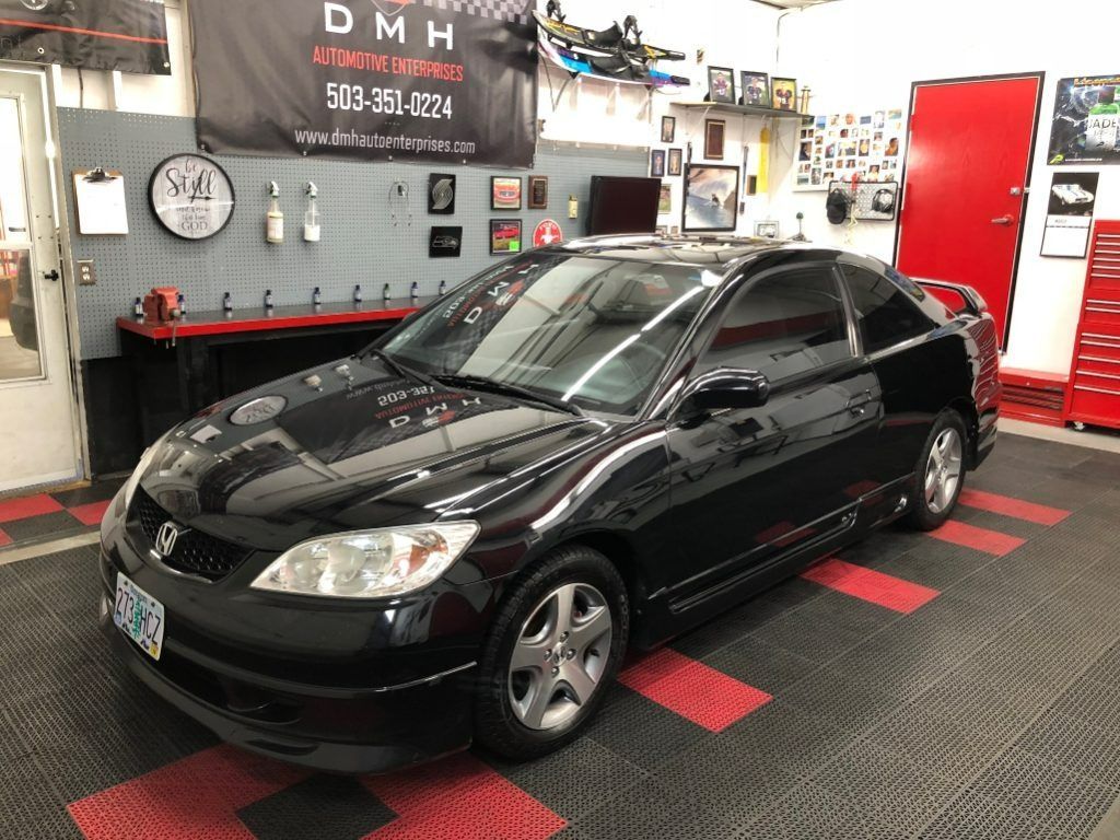 Black sedan in a workshop garage with tools, wall clock, and red door in the background