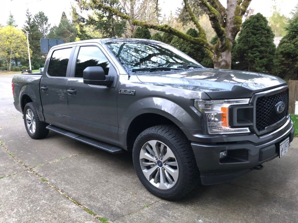 Gray Ford pickup truck parked on a driveway with trees and shrubs in the background
