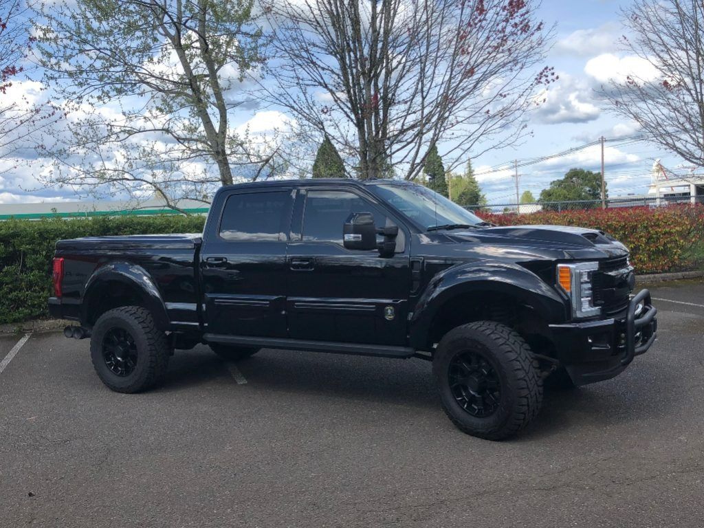 Black lifted pickup truck parked on pavement near trees under a partly cloudy sky