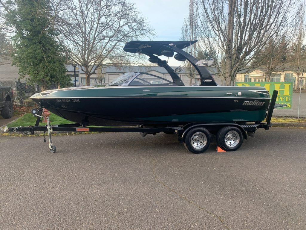 Dark green motorboat on a trailer parked on a road, with trees and houses in the background