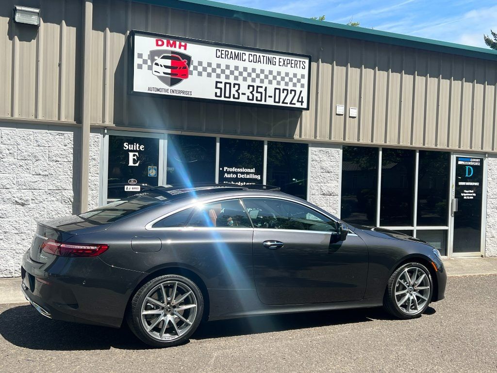 Gray sports coupe parked outside a shop with a banner sign and bright sun glare on the windows