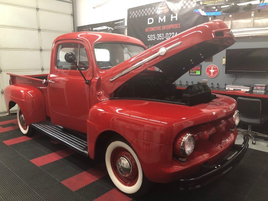 Red vintage pickup truck with hood open in a showroom, glossy finish and whitewall tires