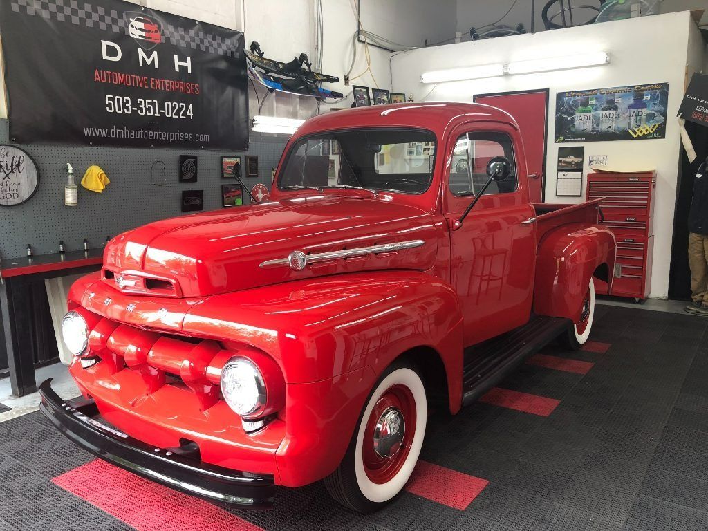 Bright red vintage pickup truck in a garage showroom, with whitewall tires and chrome details.