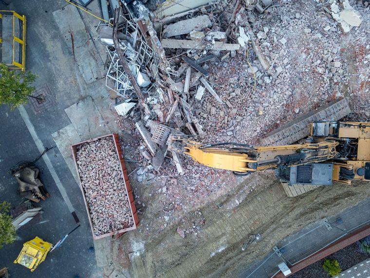 Aerial view of a yellow excavator clearing rubble in a demolition site beside a road