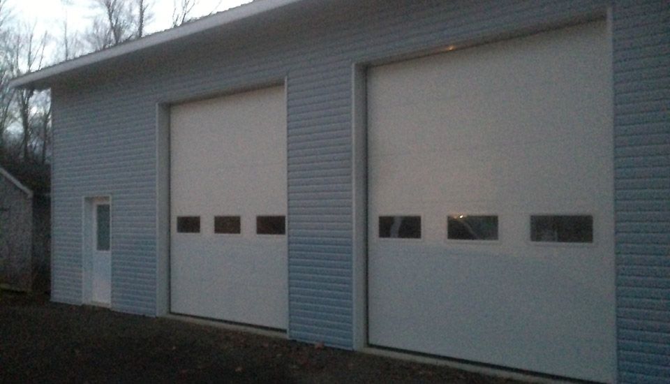 Building with two large garage doors and a small door, light blue siding.