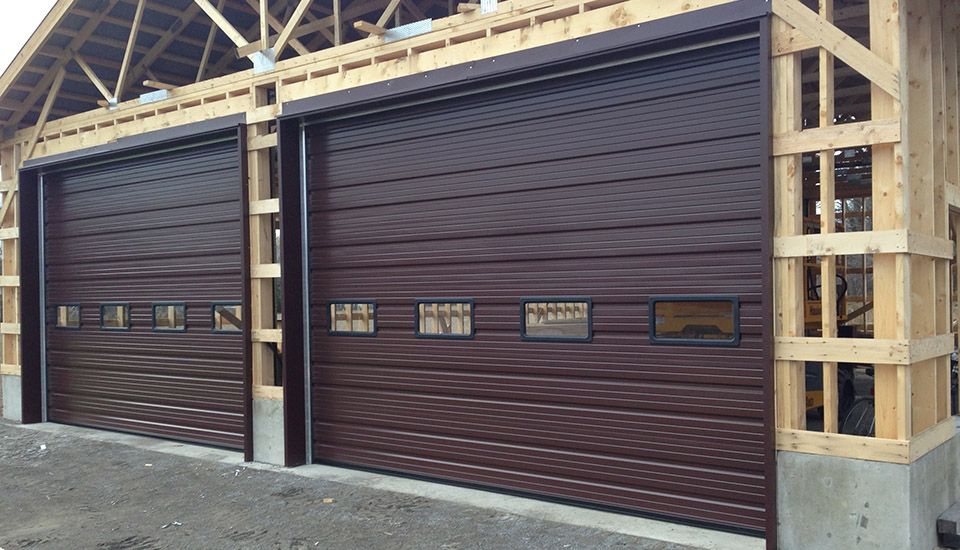 Two brown garage doors in a wooden building under construction.
