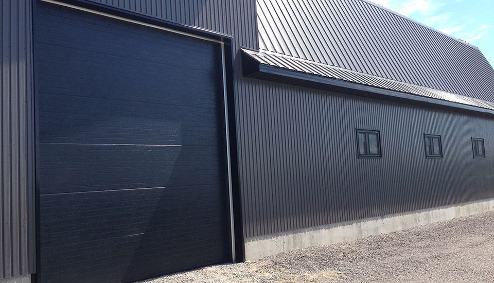 Black building with large door, metal siding and roof, small windows.