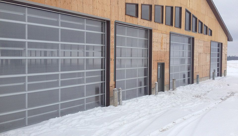 Wooden building with transparent garage doors, snowy ground.