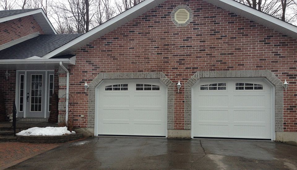 Brick house exterior with two white garage doors and a front door.