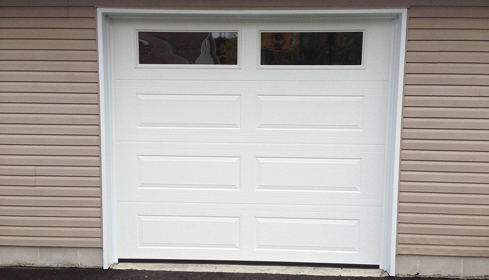 White garage door with two upper windows, set in a tan siding wall.