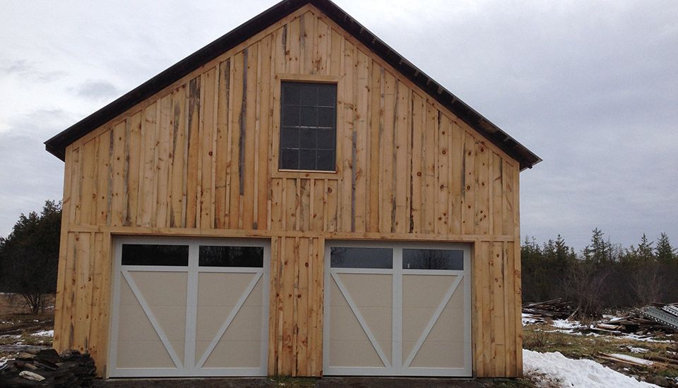 Wooden two-car garage with white doors, window above, and snow-covered ground.