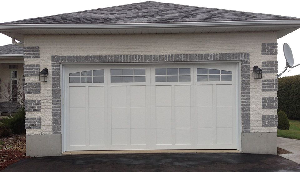 White garage door with glass paneling, surrounded by brick and stone, driveway.
