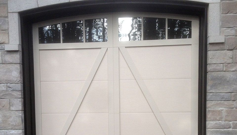Beige garage door with arched glass panel, set in a stone wall.