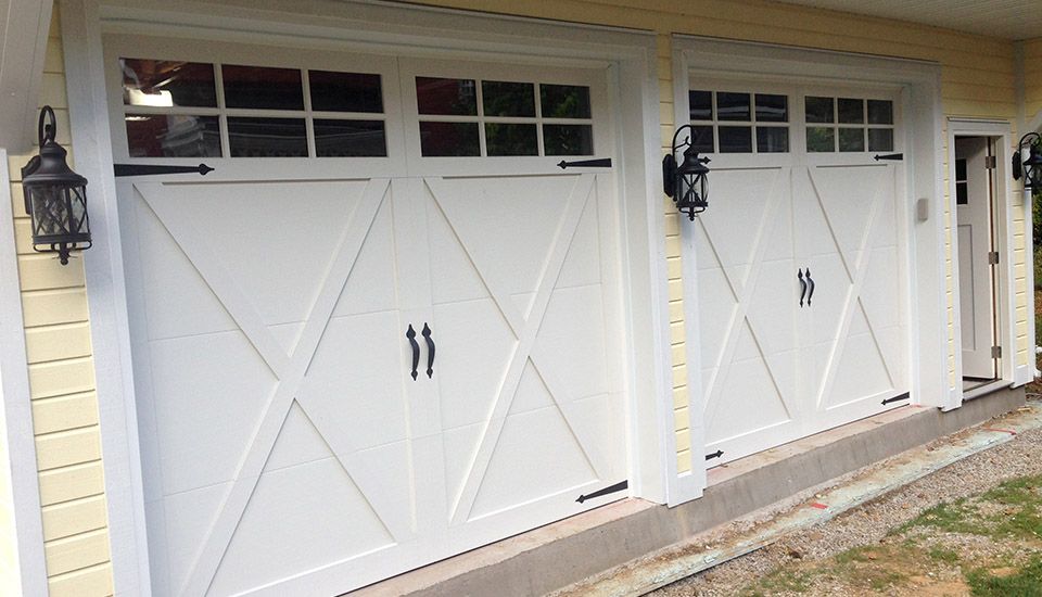 White garage doors with black hardware and windows, yellow exterior.