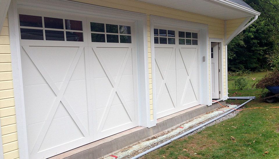 White garage doors with cross design and windows, yellow siding, and green grass.