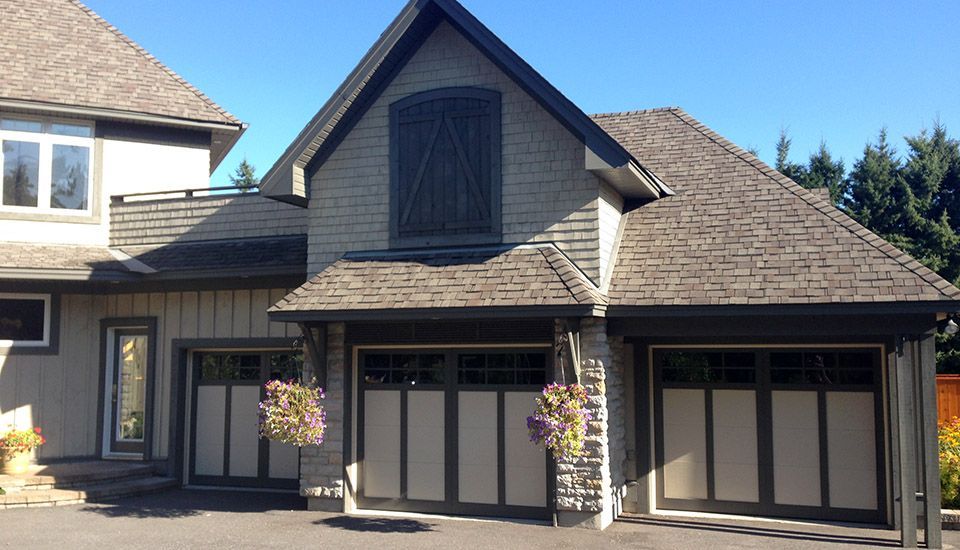 Tan and gray stone house with three-door garage; pink hanging flowers, blue sky.