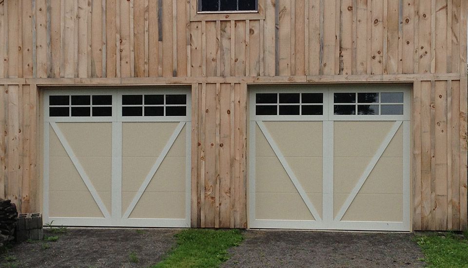 Two tan and white garage doors with windows in a wood-paneled barn.