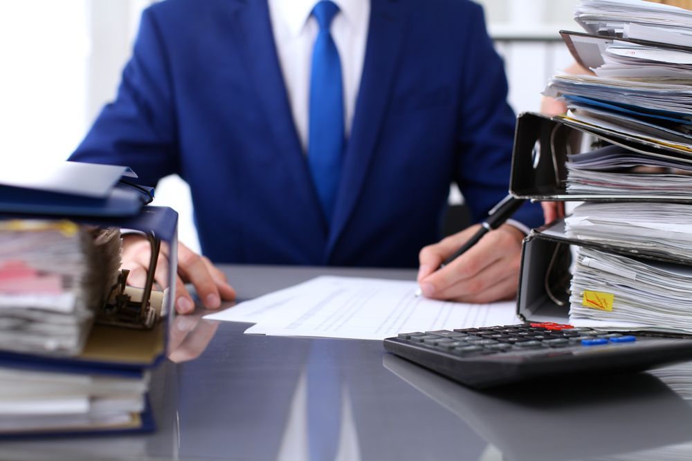 Man in Blue Suit at Desk, Surrounded by Paperwork
