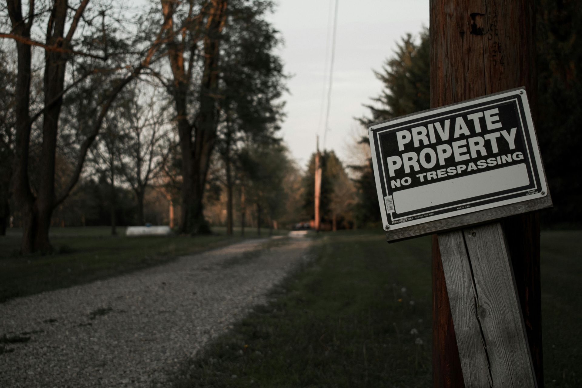 Private property no trespassing sign beside a gravel road at dusk