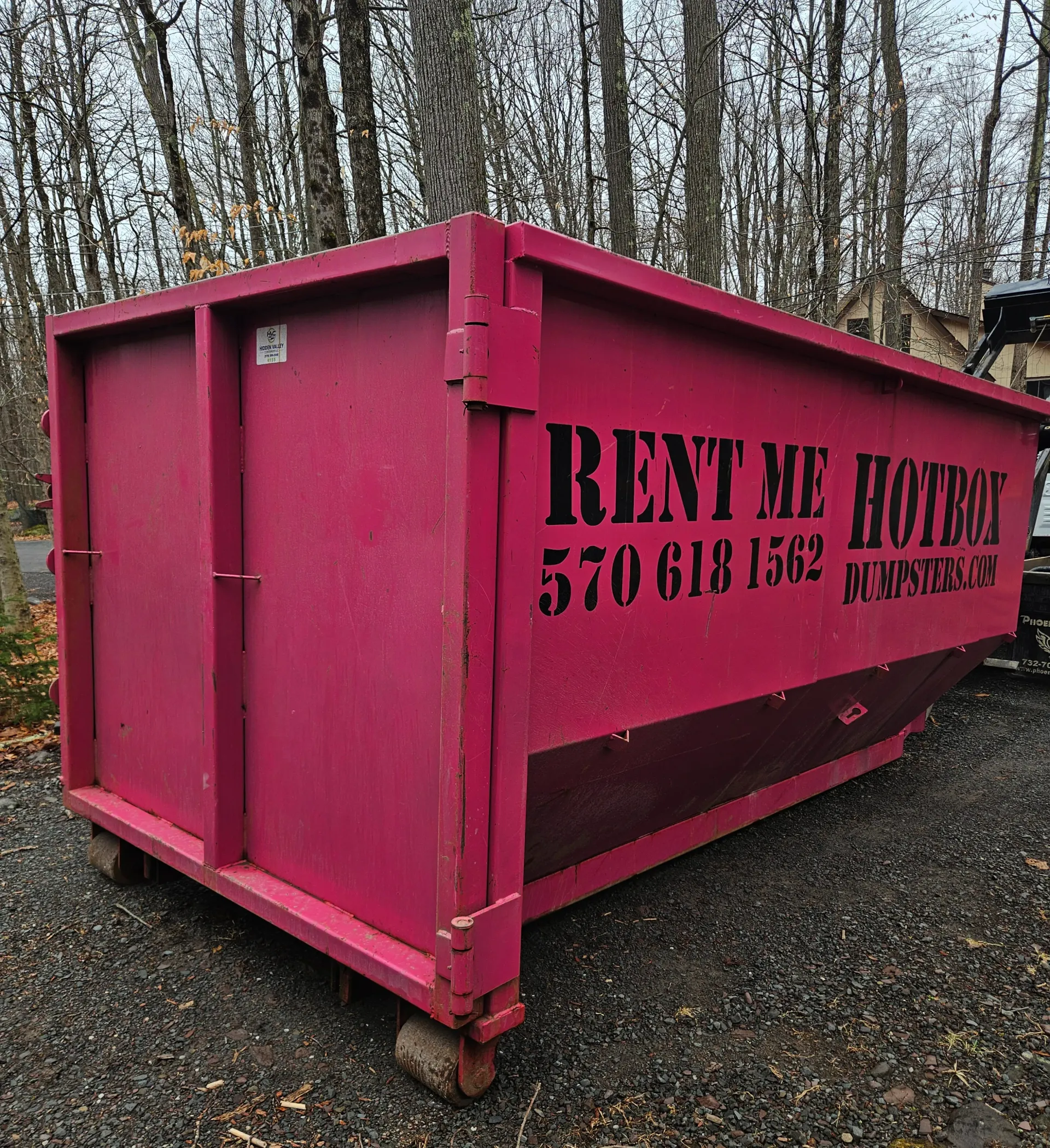 A dumpster is being towed by a truck in front of a building.