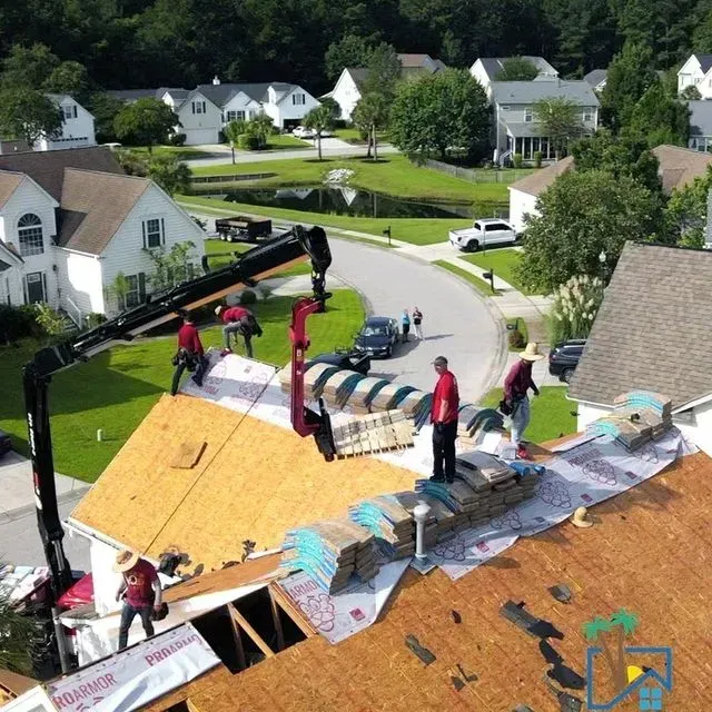 Roofers replacing a roof on a house in a suburban neighborhood. A crane lifts materials.