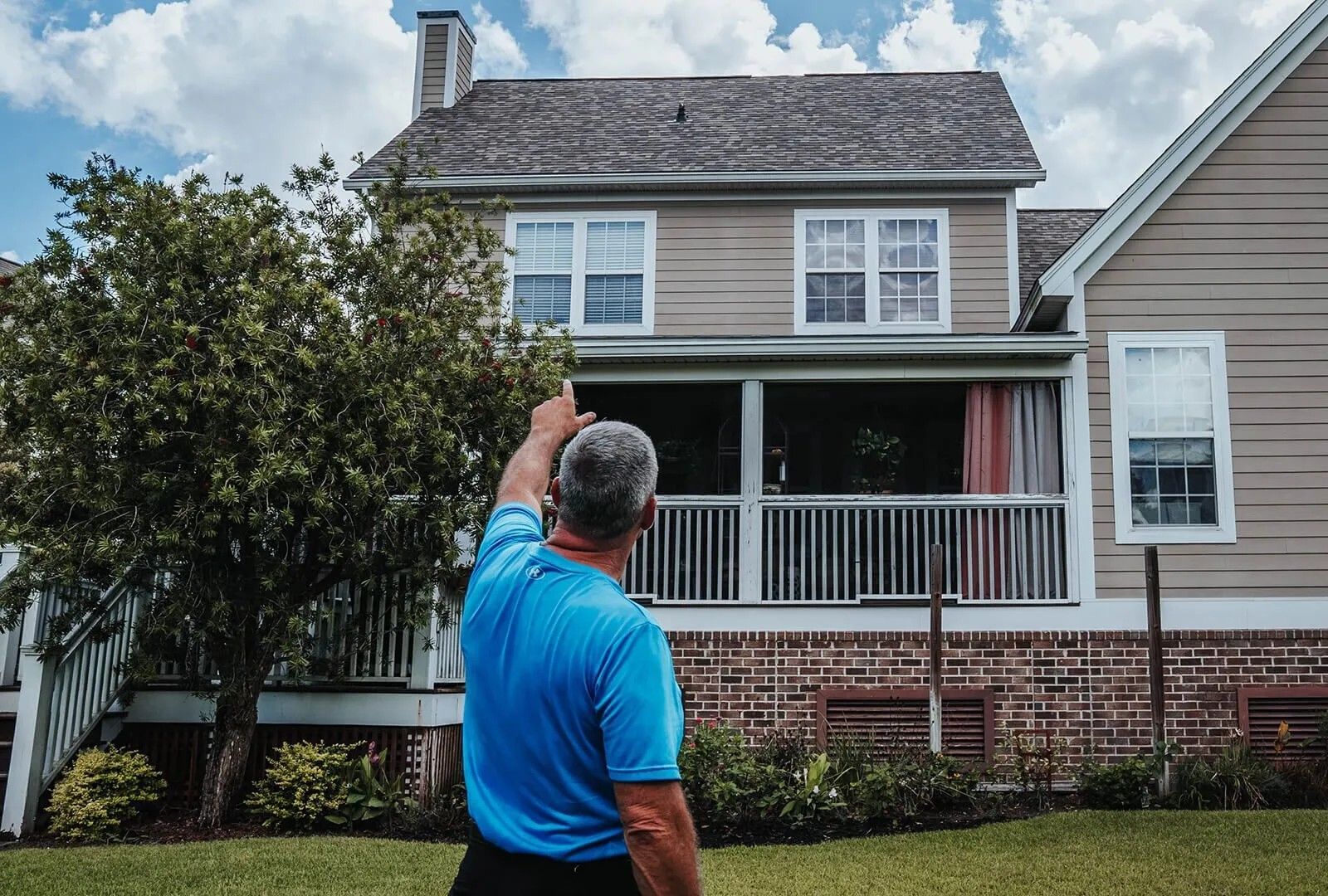Man pointing upward at two-story house with porch; green lawn, blue sky. Man pointing upward at two-story house with porch; green lawn, blue sky.